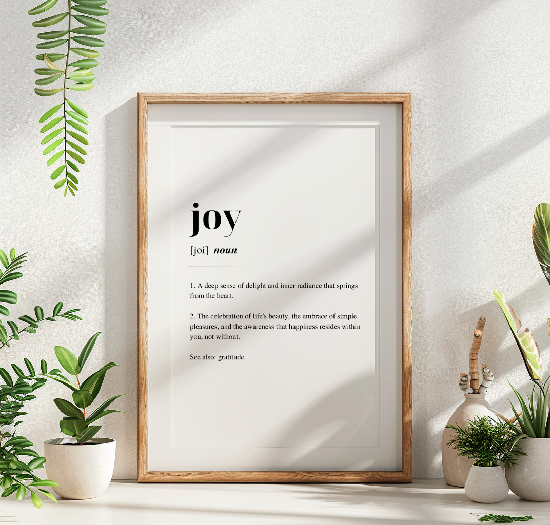 Wooden framed poster with inspirational definition art text for the word and meaning of Joy. the frame is surrounded by plants against a white wall