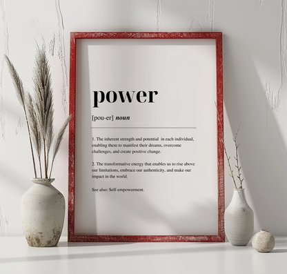 A digital art print with the word 'POWER' written in black capital letters, defined as 'the ability to transform weakness into strength and to face challenges with determination'. The print is framed in a red enclosure, displayed on a white wall, with a vase with dried flowers to the left and a vase with fresh flowers to the right.