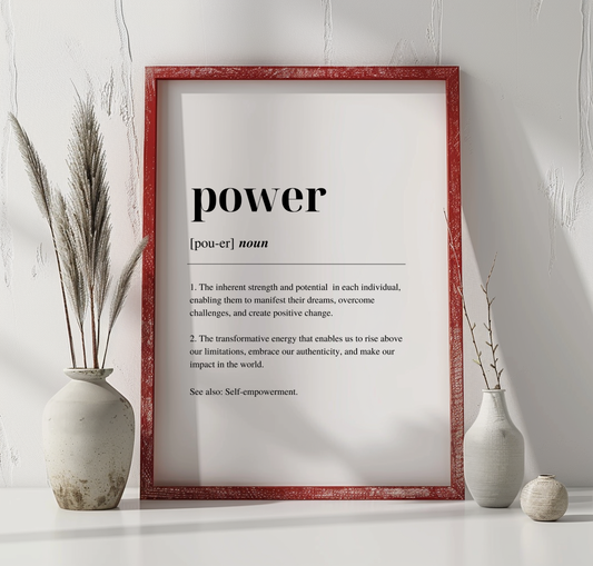 A digital art print with the word 'POWER' written in black capital letters, defined as 'the ability to transform weakness into strength and to face challenges with determination'. The print is framed in a red enclosure, displayed on a white wall, with a vase with dried flowers to the left and a vase with fresh flowers to the right.